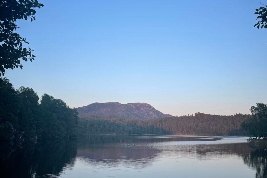 Lago tranquillo a Valevåg, in Vestland, circondato da foresta e colline, con riflessi sull’acqua al tramonto