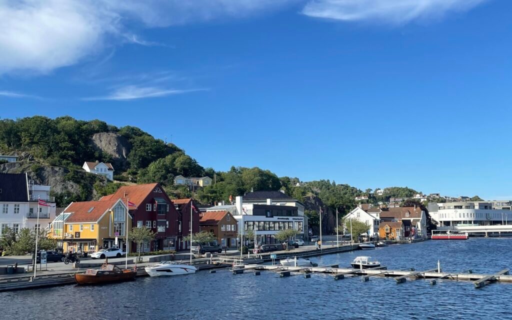 Lungo il fiume Mandalselva a Mandal, con case colorate sul lungofiume, barche ormeggiate e cielo sereno