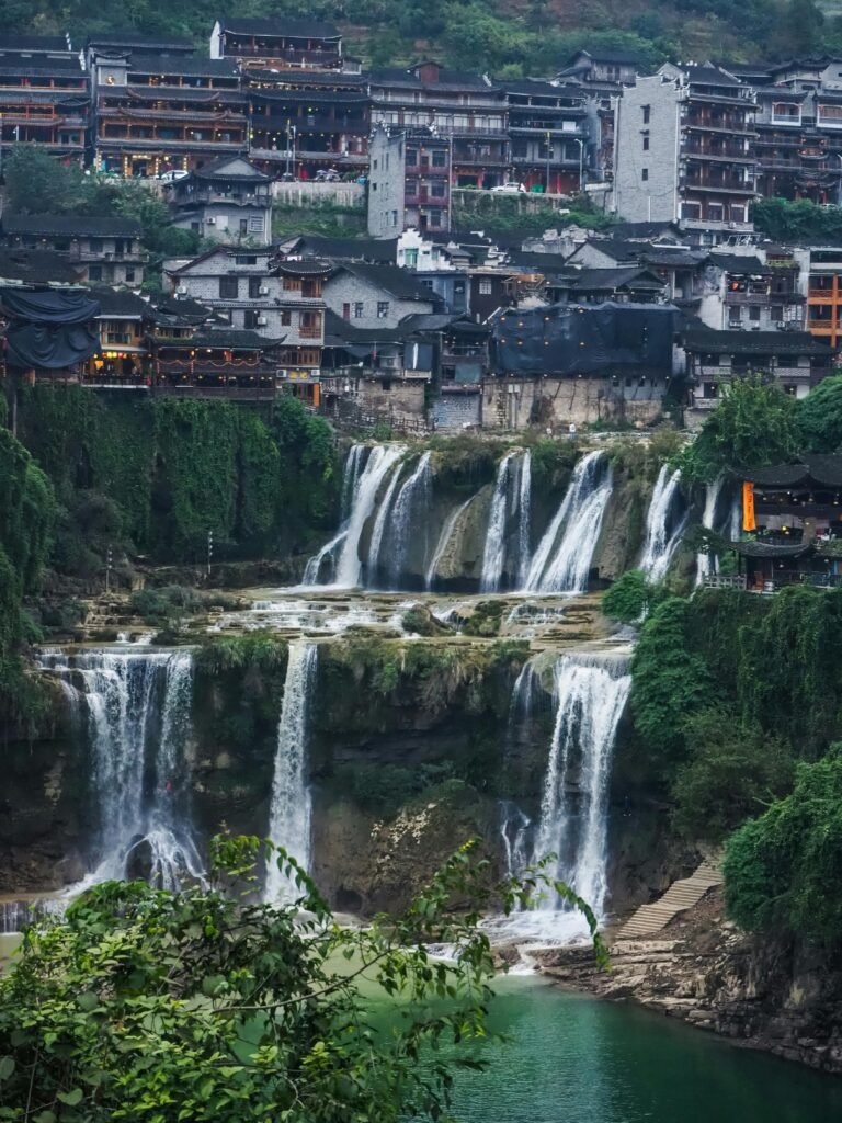 Picturesque view of waterfalls cascading in Furong Ancient Town, Hunan, China, showcasing natural beauty and architecture.